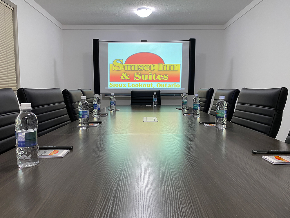 Boardroom with a long table, black chairs, and a projector screen at Sunset Inn and Suites in Sioux Lookout